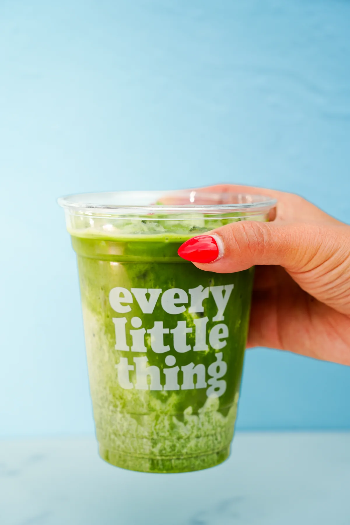 A hand holds a bright green drink against a blue background