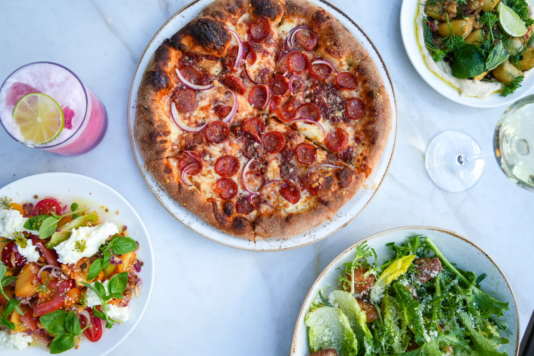 Overhead food photography of pizza, salads and drinks arranged across a restaurant table